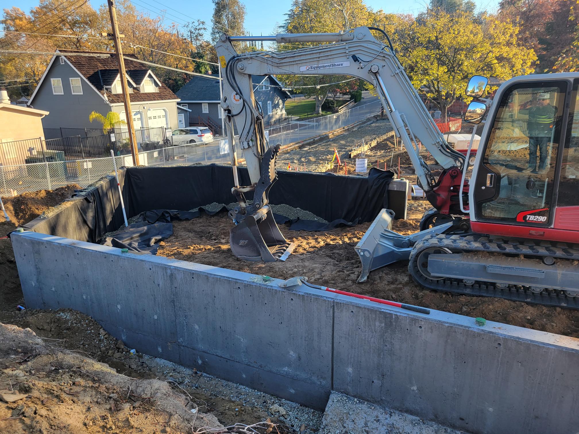 construction vehicle scooping dirt around a concrete wall